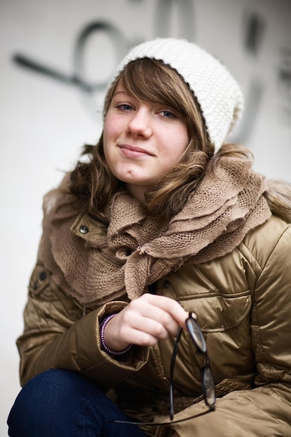 Adolescente portant un chapeau en tricot blanc et tenant des lunettes à la mode