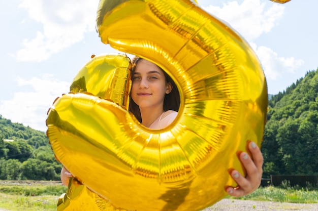 Adolescente regardant à travers des ballons dorés à huis clos. Portrait nature en plein air