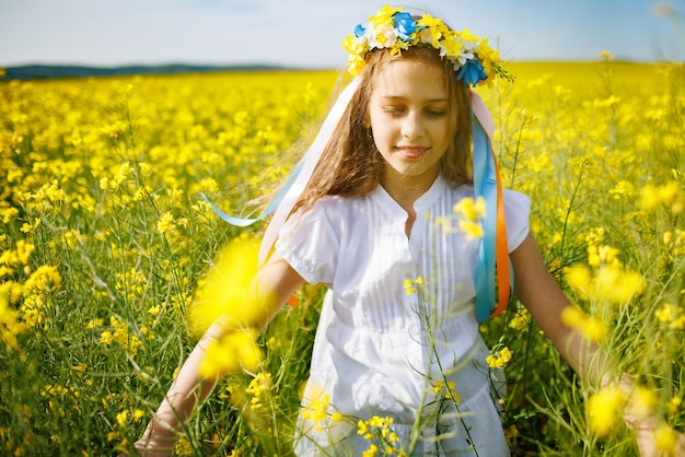 Adolescente en robe et couronne ukrainienne avec des lentims sur la tête dans un champ de colza sous un ciel bleu clair