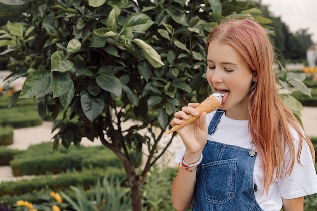 Adolescente en robe denim mangeant de la crème glacée chaude journée d'été, photo