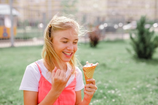 Adolescente en robe d'été assis sur l'herbe en train de manger des glaces