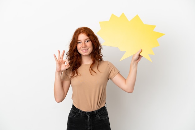 Adolescente rousse isolée sur fond blanc tenant une bulle vide et faisant signe OK