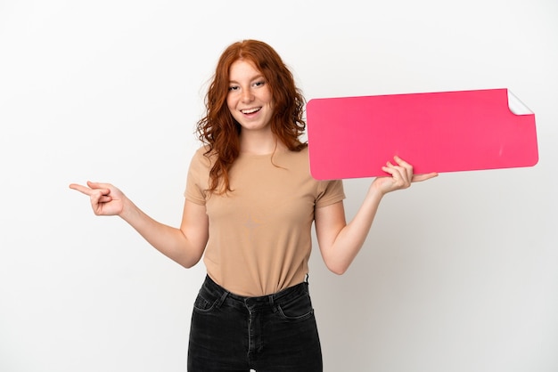 Adolescente rousse isolée sur fond blanc tenant une pancarte vide et pointant du côté