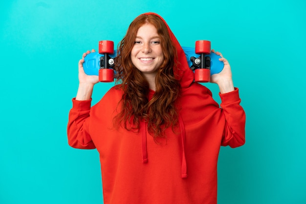 Adolescente rousse isolée sur fond bleu avec un patin avec une expression heureuse