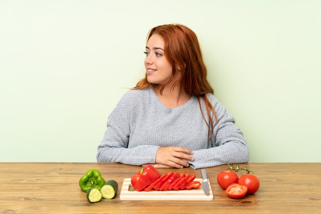 Adolescente rousse avec des légumes dans une table à la recherche du côté