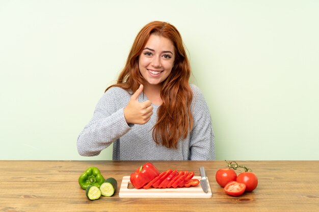 Adolescente rousse avec des légumes dans un tableau donnant un coup de pouce geste