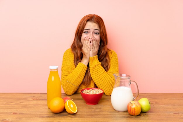 Adolescente rousse prenant son petit déjeuner dans une table avec une expression faciale surprise