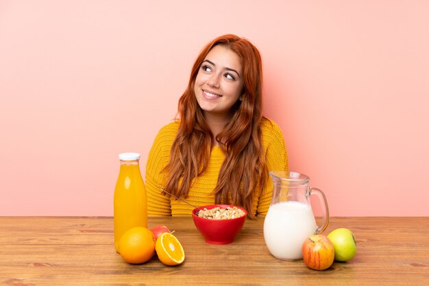 Adolescente rousse prenant son petit déjeuner dans une table en riant et levant les yeux