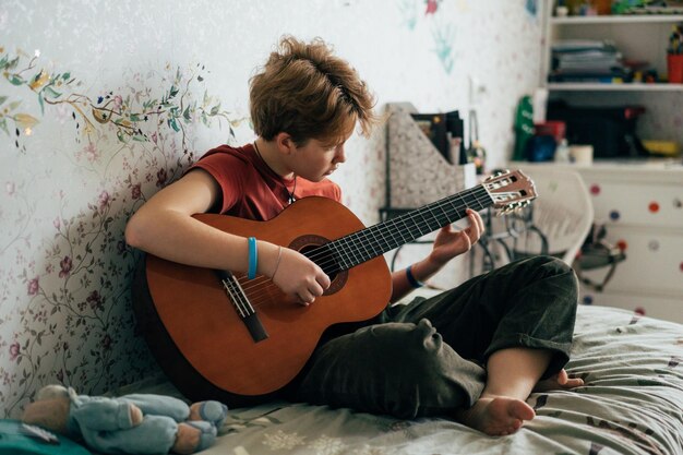 Une adolescente rousse romantique apprenant à jouer de la guitare assise dans la pièce.