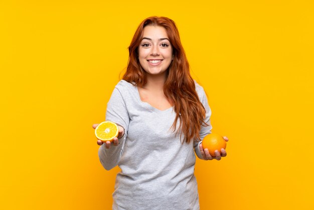 Adolescente Rousse Tenant Une Orange Sur Fond Jaune Isolé