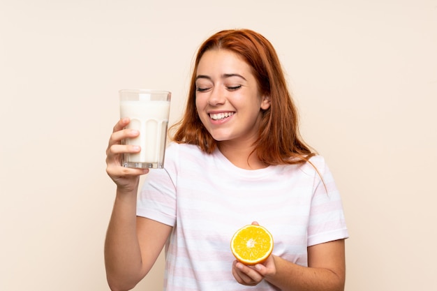 Adolescente rousse tenant un verre de lait et une orange sur un mur isolé