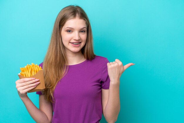 Adolescente russe attrapant des frites isolées sur fond bleu pointant vers le côté pour présenter un produit