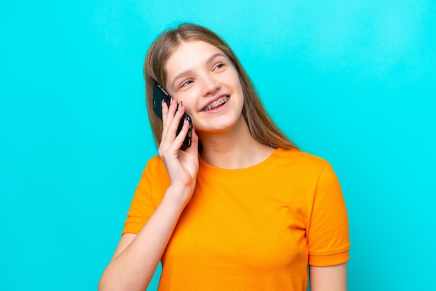 Adolescente russe isolée sur fond bleu en gardant une conversation avec le téléphone portable avec quelqu'un