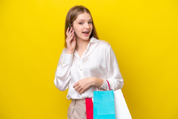 Adolescente russe isolée sur fond jaune tenant des sacs à provisions et appelant un ami avec son téléphone portable