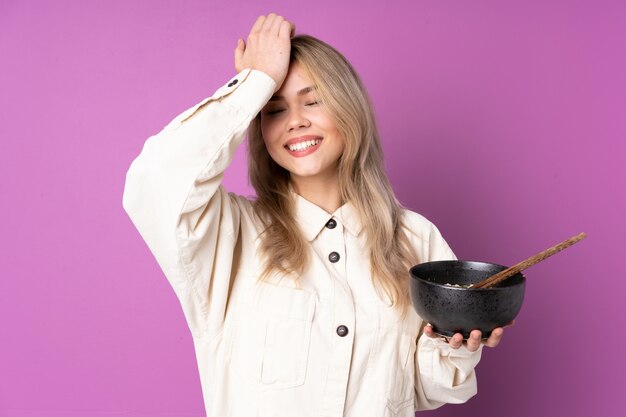 Une adolescente russe sur un mur violet a réalisé quelque chose et a l'intention de trouver la solution tout en tenant un bol de nouilles avec des baguettes