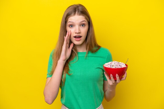 Adolescente russe tenant un bol de céréales isolé sur fond jaune avec une expression faciale surprise et choquée