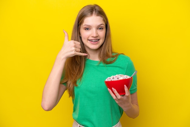 Adolescente russe tenant un bol de céréales isolé sur fond jaune faisant un geste de téléphone Call me back sign