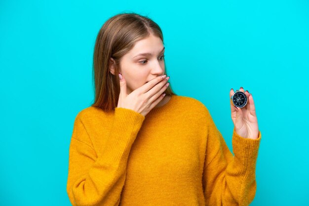 Adolescente russe tenant une boussole isolée sur fond bleu avec une expression faciale surprise et choquée