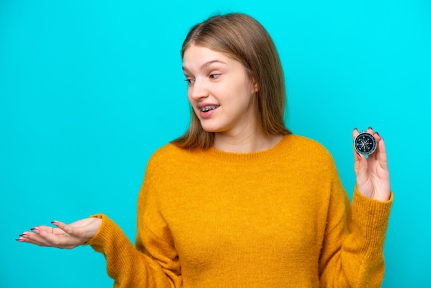 Adolescente russe tenant une boussole isolée sur fond bleu avec une expression faciale surprise