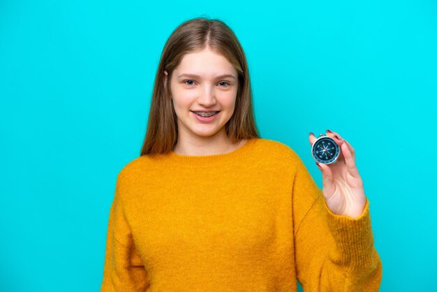 Adolescente russe tenant une boussole isolée sur fond bleu avec une expression heureuse