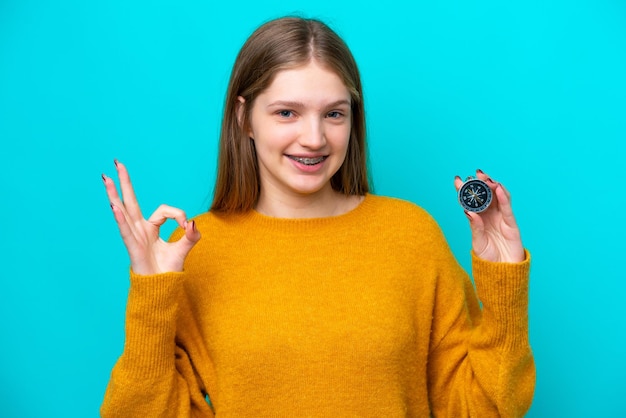 Adolescente russe tenant une boussole isolée sur fond bleu montrant un signe ok avec les doigts