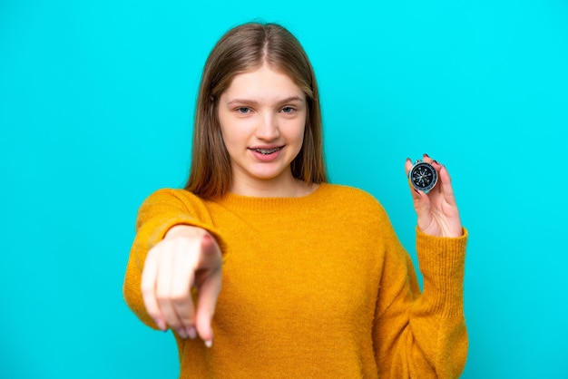 Adolescente russe tenant une boussole isolée sur fond bleu pointe le doigt vers vous avec une expression confiante