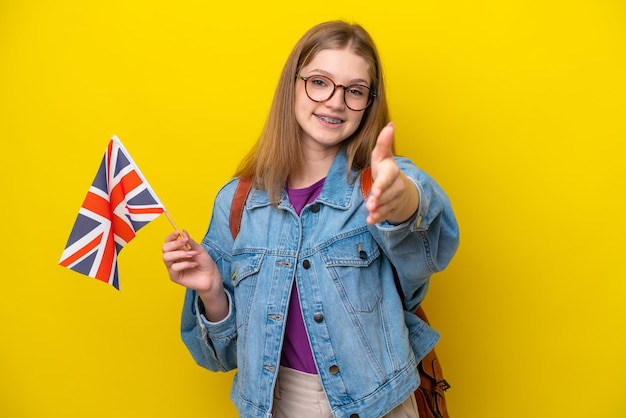 Adolescente russe tenant un drapeau du Royaume-Uni isolé sur fond jaune se serrant la main pour conclure une bonne affaire