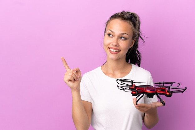 Une adolescente russe tenant un drone isolé sur fond violet dans l'intention de réaliser la solution tout en levant un doigt vers le haut