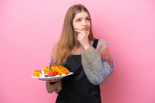 Adolescente russe tenant une gaufre isolée sur fond rose ayant des doutes