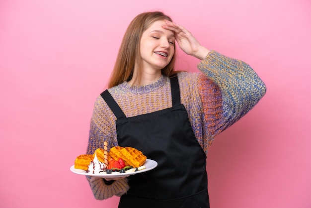 Adolescente russe tenant une gaufre isolée sur fond rose souriant beaucoup