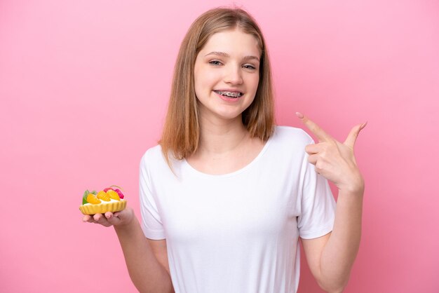 Adolescente russe tenant une tartelette isolée sur fond rose donnant un geste du pouce levé