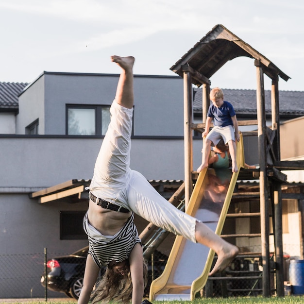 Photo une adolescente s'entraîne à faire du cartwheel contre son frère sur une toboggan dans une aire de jeux.