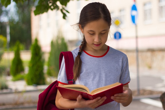 Une adolescente se tient près de l'école en lisant un livre Concept de retour à l'école, mise au point sélective