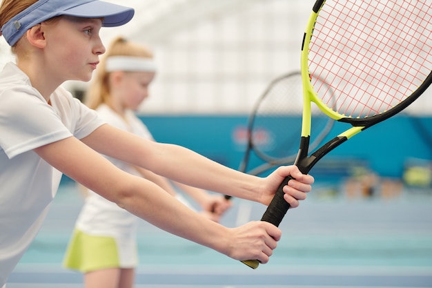 Adolescente sérieuse et concentrée en vêtements de sport debout sur le stade et tenant une raquette de tennis prête à pousser la balle pendant le jeu