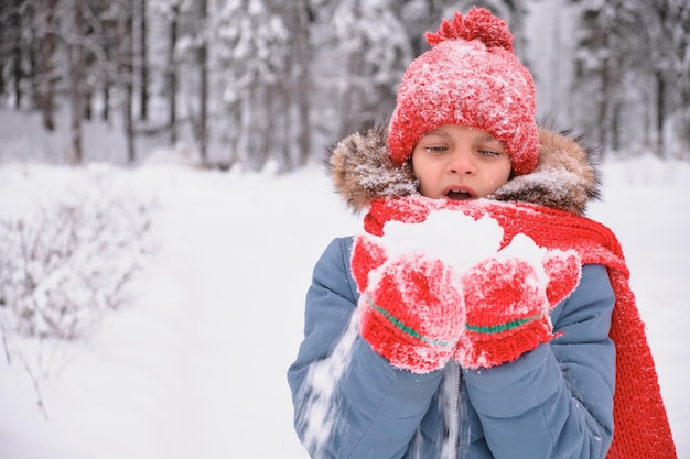 Une adolescente souffle sur la neige dans ses paumes et attise des mitaines et un bonnet tricoté changeant de temps