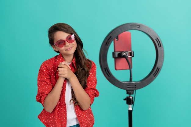 Adolescente souriante cheveux longs à lunettes de soleil parlant sur un blog vidéo de caméra blogging en ligne avec un influenceur led selfie