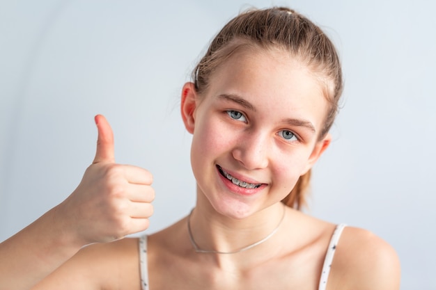 Adolescente souriante dans des brackets orthodontiques montrant le pouce vers le haut. Fille avec des accolades sur les dents. Un traitement orthodontique.