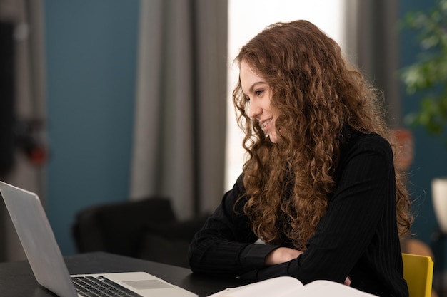 Une adolescente souriante étudie à distance La jeune fille est assise au bureau à l'aide d'un ordinateur portable