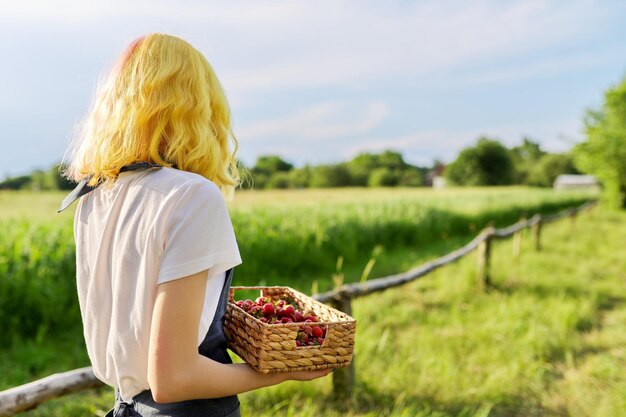 Adolescente souriante avec des fraises dans le panier jardin nature fond