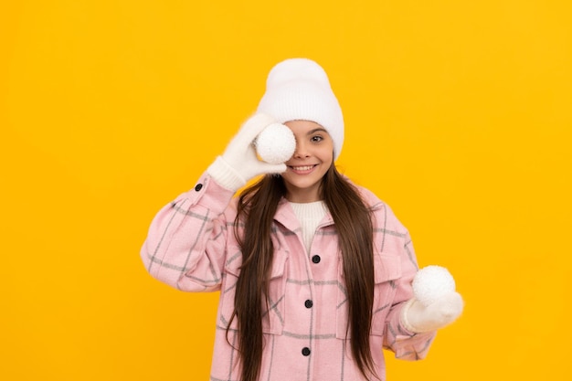 Adolescente souriante en mitaines avec boule décorative sur fond jaune