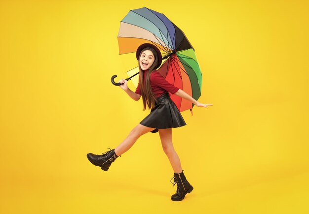 Photo adolescente sous parapluie arc-en-ciel par temps d'automne isolé sur fond jaune vêtements pour enfants d'automne adolescent excité heureux d'émotions étonnées et ravies