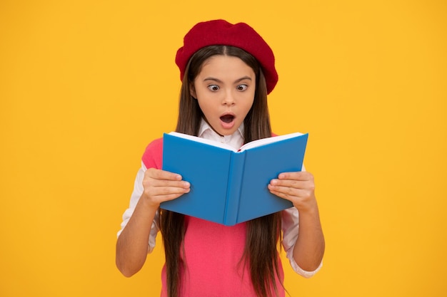 Adolescente surprise écolière en béret français lisant un livre sur fond jaune surprise