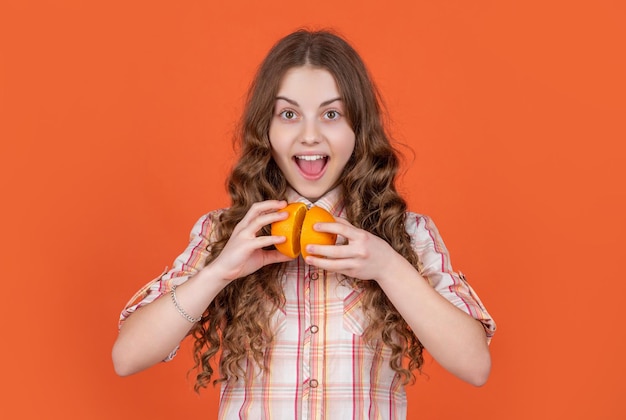 Une adolescente surprise tient des fruits citriques sur fond orange