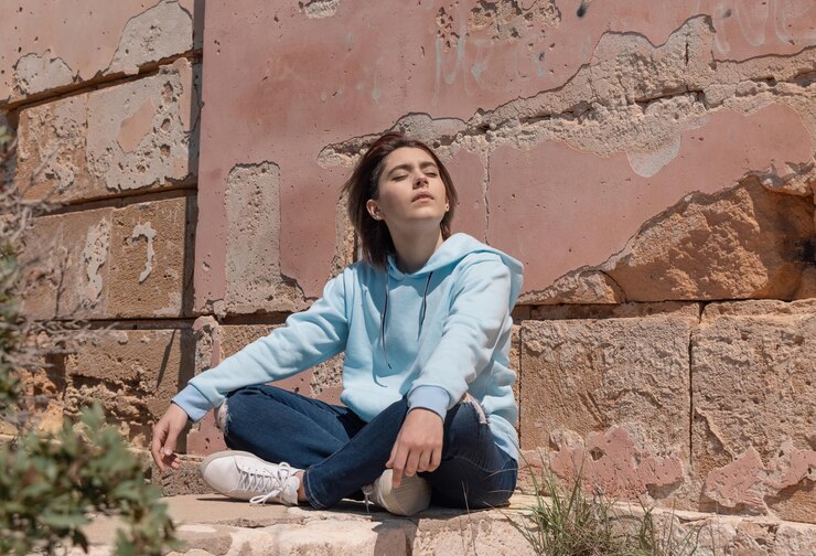 Photo adolescente en sweat à capuche bleu clair assise sur ses hanches près d'un mur