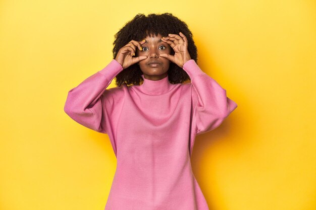 Photo une adolescente en sweat-shirt rose sur fond de studio jaune gardant les yeux ouverts pour trouver un succès