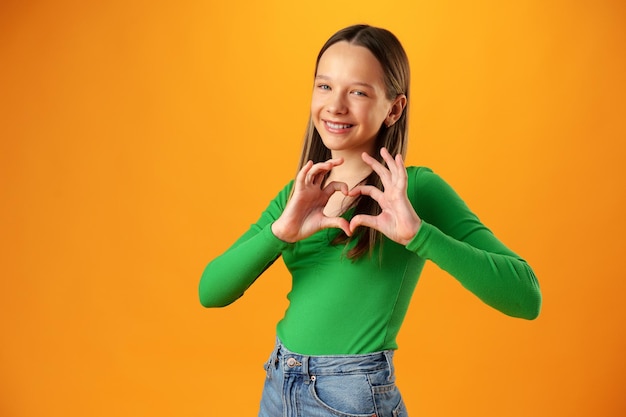 Une adolescente sympathique montre un geste d'amour de coeur sur fond jaune