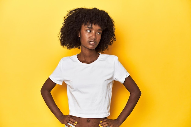 Photo une adolescente en t-shirt blanc classique, sur fond de studio jaune, confuse, se sent dubitative et incertaine