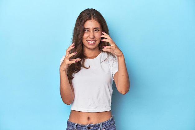 Adolescente en T-shirt blanc sur fond bleu bouleversée criant avec les mains tendues