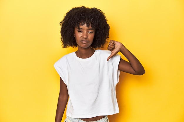 Photo une adolescente en tank-top blanc à l'arrière-plan jaune du studio montrant le pouce vers le bas concept de déception