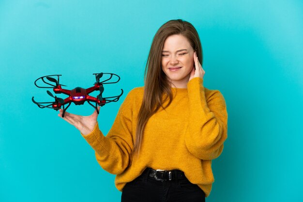 Adolescente tenant un drone sur fond bleu isolé frustré et couvrant les oreilles